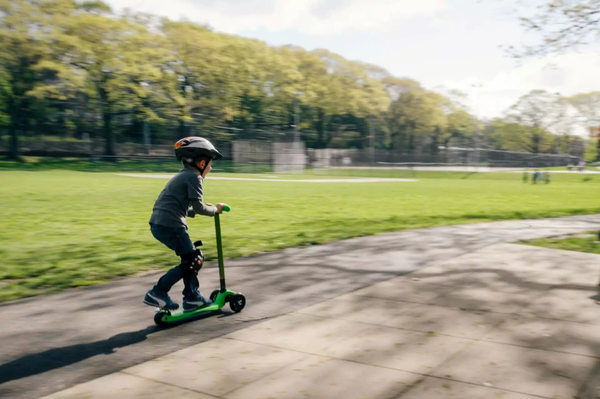 Kind fährt dynamisch mit Scooter in einer Parkanlage