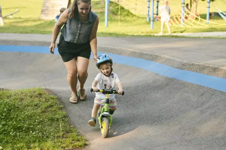 Mutter schiebt Kind auf Laufrad auf einem Pumptrack